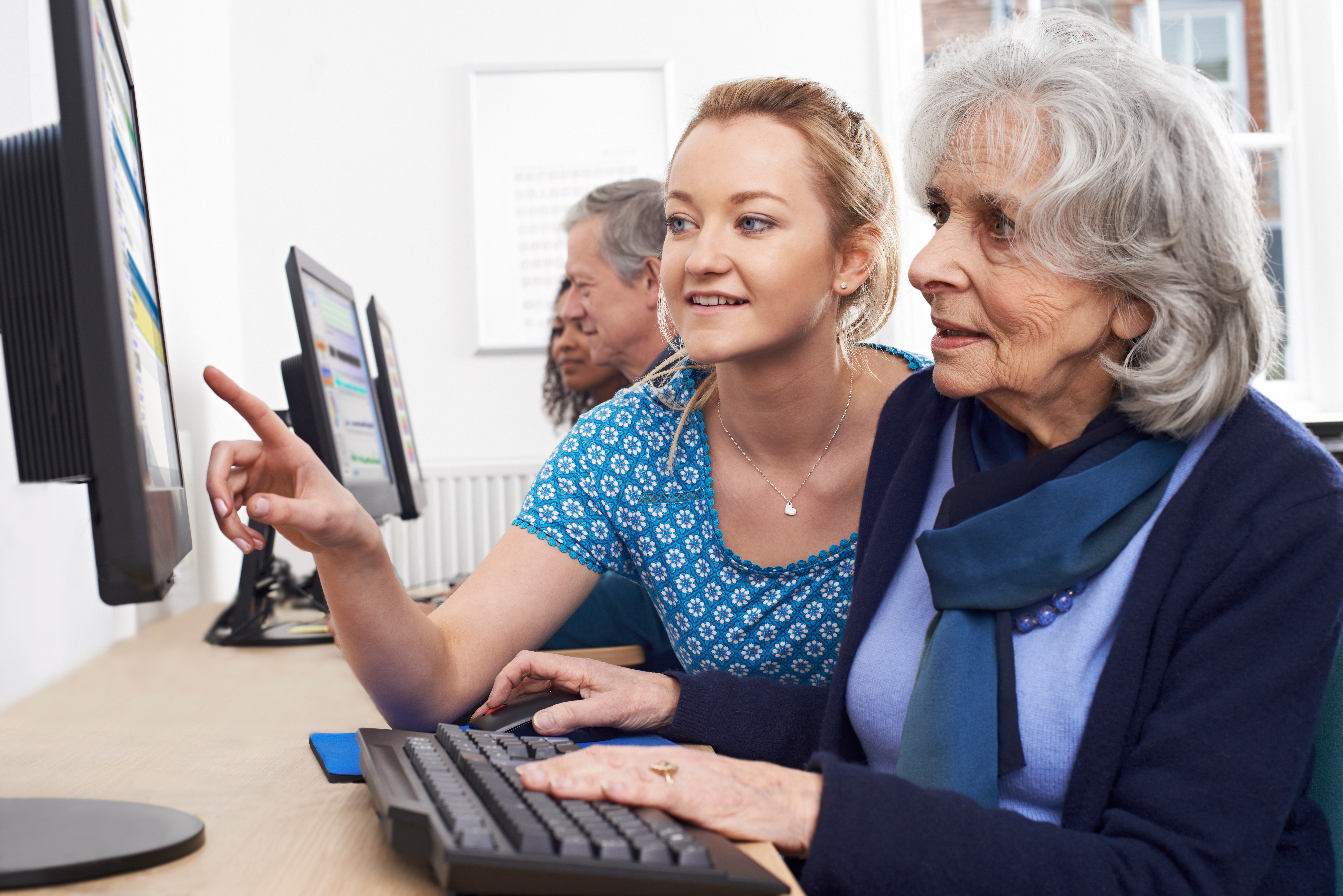 Eine ältere Dame bekommt von einer jungen Dame am PC etwas erklärt