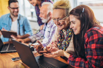 Eine Gruppe an unterschiedlichen Leuten lernen am Schreibtisch über Funktionen des Laptops