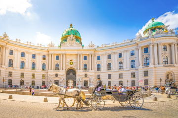 Prunkvolles Wiener Gebäude, davor ein fahrender Fiaker.