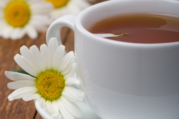 Eine Teetasse, daneben Gänseblümchen.