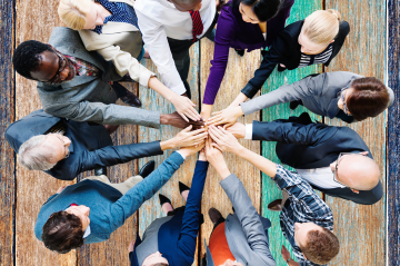 Eine Gruppe steht zusammen im Kreis und alle halten die Hand nach vorne. 